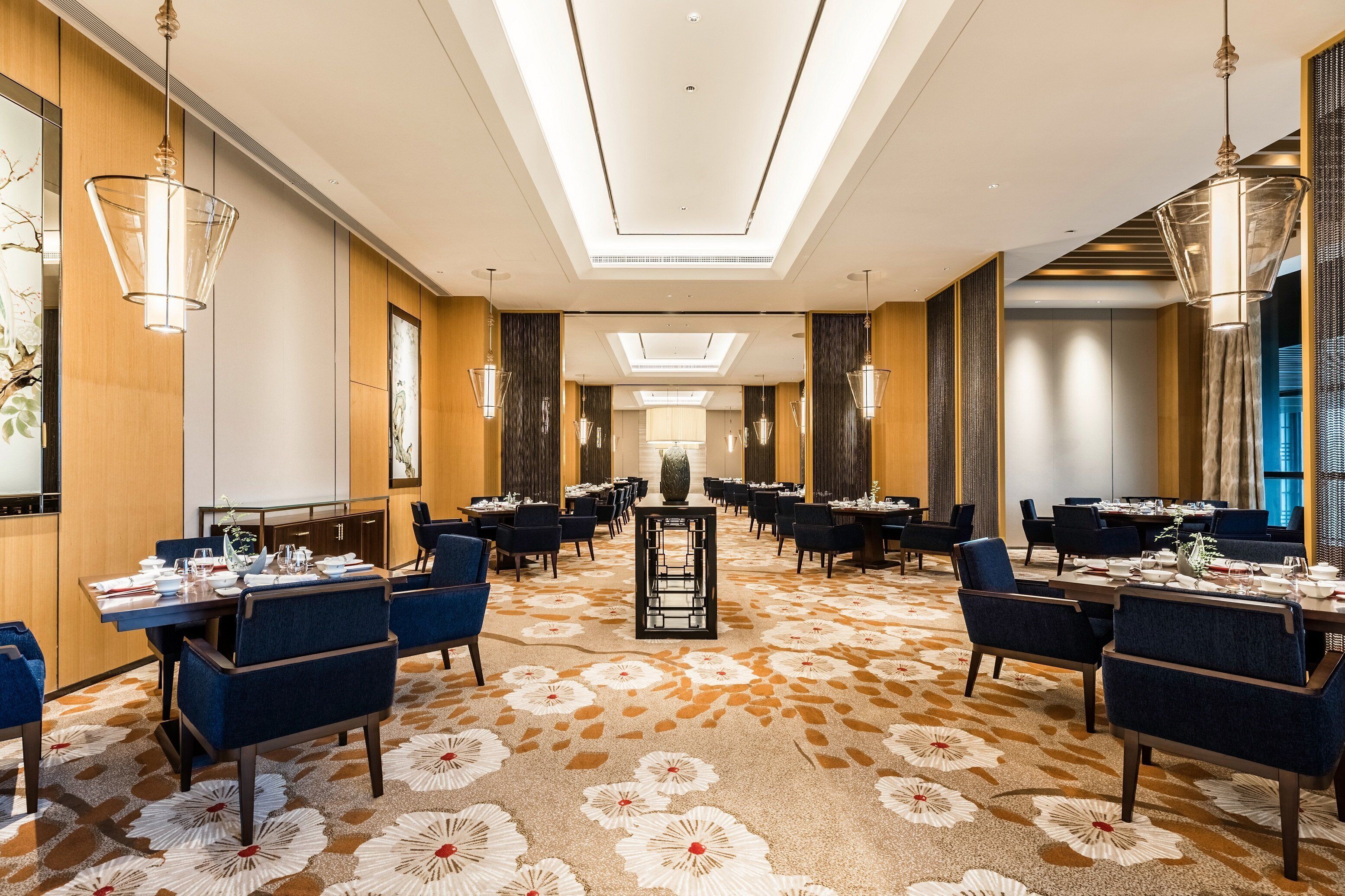 A hotel dining area with tables set for service, a central decorative piece, and a patterned carpet.