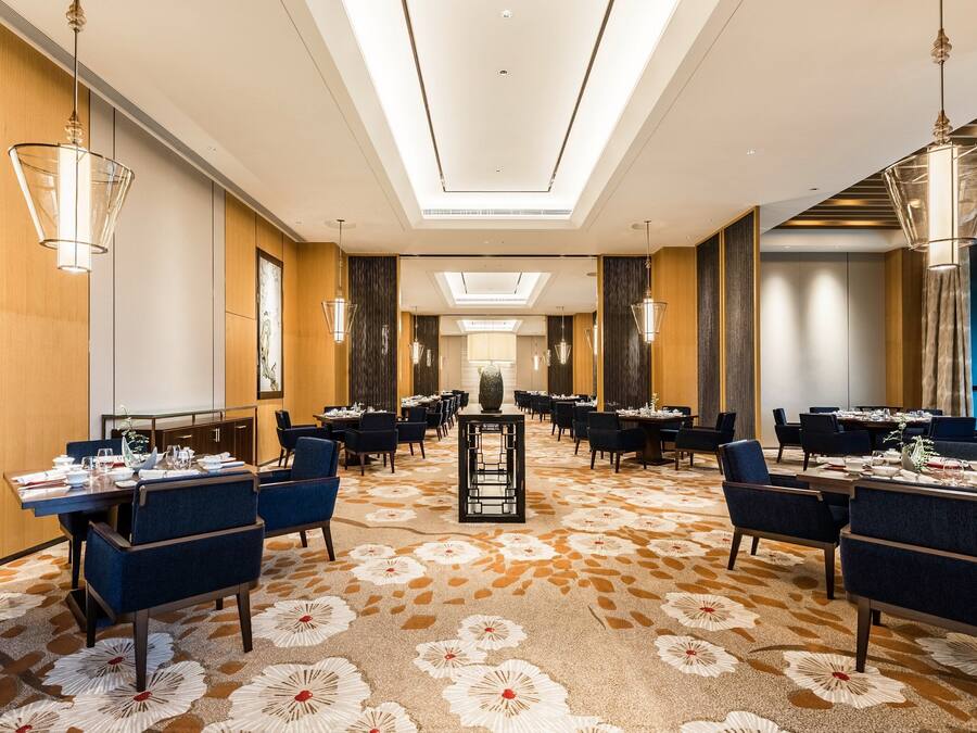 A hotel dining area with tables set for service, a central decorative piece, and a patterned carpet.