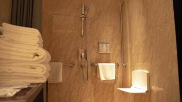 A bathroom with a marble wall, a towel rack with folded towels, a handheld showerhead, a handheld shower, and a towel warmer.