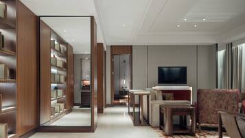 A modern hotel room with a large mirror, built-in wooden shelving, a flat-screen TV, and a cozy seating area.