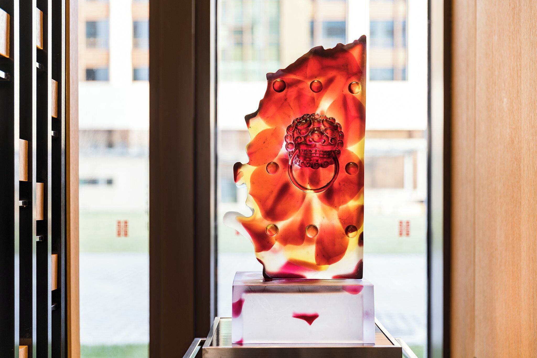 A sculpture of a face with a crown, placed on a pedestal in front of a window.