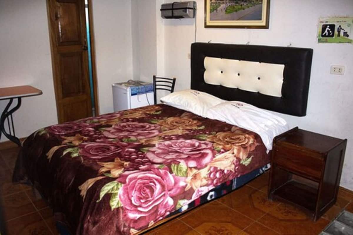 A bed with a floral bedspread, a wooden headboard, a bedside table, and a chair.