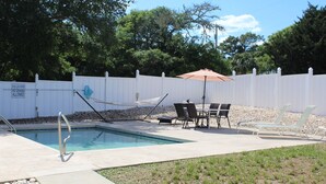 A swimming pool with a white fence, lounge chairs, and a table with an umbrella. - Beach House with Pool - Pet Friendly (North Myrtle Beach)
