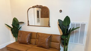 A brown leather sofa with a mirror above it, flanked by large green plants.