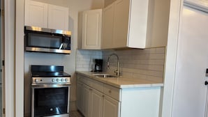A compact kitchen with white cabinets, a built-in microwave, a gas stove, and a coffee maker.
