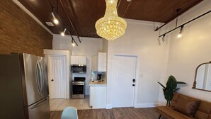 A modern kitchen with stainless steel appliances, a dining area with a table and chairs, and a living area with a sofa and a plant.