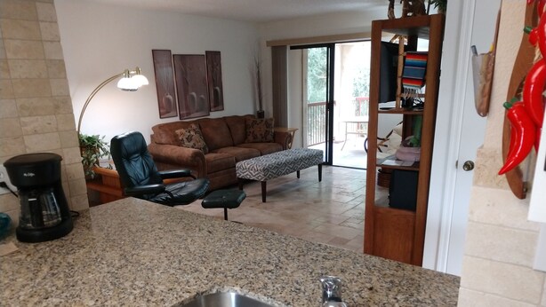 A kitchen with granite countertops, a stainless steel sink, and a dining area with a brown leather couch and a patterned ottoman. - Beautifully furnished condo at the Villages in McCormick Ranch Scottsdale, AZ (Scottsdale)