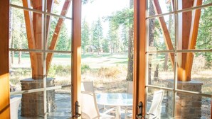 A glass-enclosed patio with a stone fireplace, a round table, and chairs, overlooking a golf course. - Golf Course View w/ Suncadia Pool Access (Cle Elum)