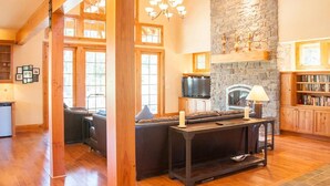 A cozy living room with a stone fireplace, wooden beams, and a large window. - Golf Course View w/ Suncadia Pool Access (Cle Elum)