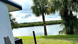 A patio with a round table and chairs, a small white pedestal table with a potted plant, and a grill. - Home Base for New Smyrna Adventures (New Smyrna Beach)