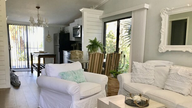 A spacious living room with two white sofas, a wooden coffee table, and a chandelier. - Home Base for New Smyrna Adventures (New Smyrna Beach)