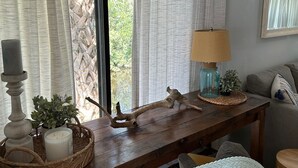 A wooden table with decorative items, a lamp, and a view of greenery outside. - Home Base for New Smyrna Adventures (New Smyrna Beach)