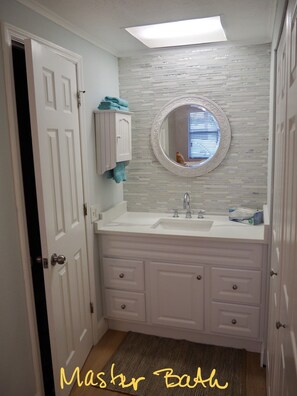 Features a white vanity with a round mirror and two cabinets, a small window, and a towel.