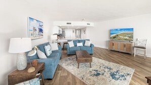 Ein Wohnzimmer mit blauem Sofa, Holztisch und einem Gemälde mit Strandmotiv.