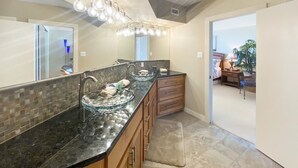Un baño moderno con un tocador espacioso, un lavabo de vidrio y una ducha a pie.