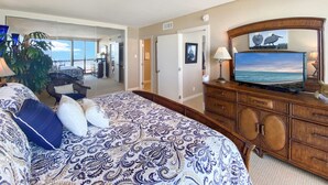 Habitación de hotel con una cama grande, televisor, cómoda de madera y vista al océano.