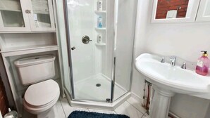 A bathroom with a toilet, a glass-enclosed shower, a sink, and a cabinet.