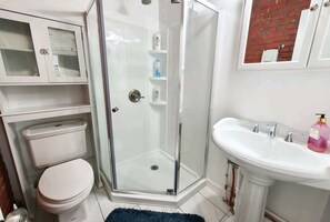 Modern bathroom with a glass-enclosed shower, pedestal sink, and toilet.