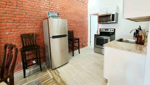 A compact kitchen with a brick wall, a refrigerator, a microwave, an oven, and a sink.