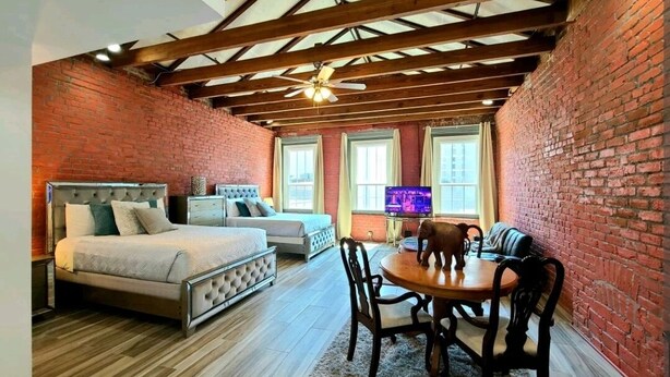 A bedroom with a bed, a TV, and a dining area with chairs.