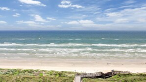 Ein Strand mit einer Holzpromenade, die zu einem Gebäude führt, mit Blick auf den Ozean.