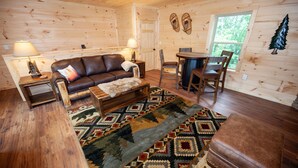 A cozy cabin interior with a wooden floor, a leather sofa, a patterned rug, and a dining area with chairs and a table. - Quiet Mountain Top Family Cabin- Private, Top Location, VIEWS! (Sevierville)