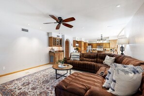 Un salon spacieux avec un grand canapé d’angle en cuir marron, une table basse et un ventilateur de plafond.