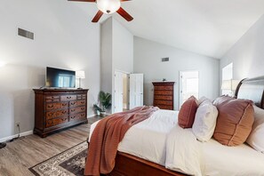 Une chambre à coucher comprenant un lit, une commode en bois, un ventilateur de plafond et un téléviseur.