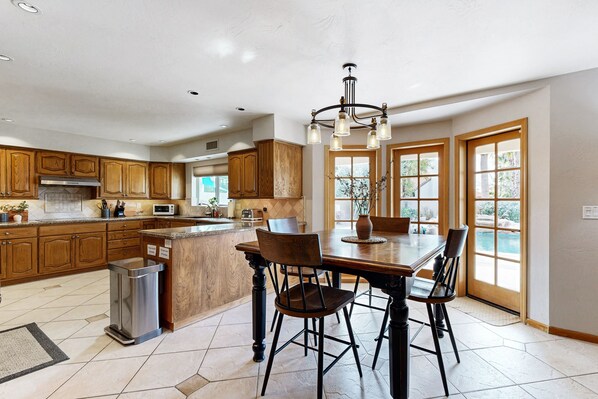 A spacious kitchen with wooden cabinets, a central island, and a dining area with chairs. - Gorgeous home with private pool, outdoor TV, bikes, foosball, jetted tub, & W/D (Scottsdale)