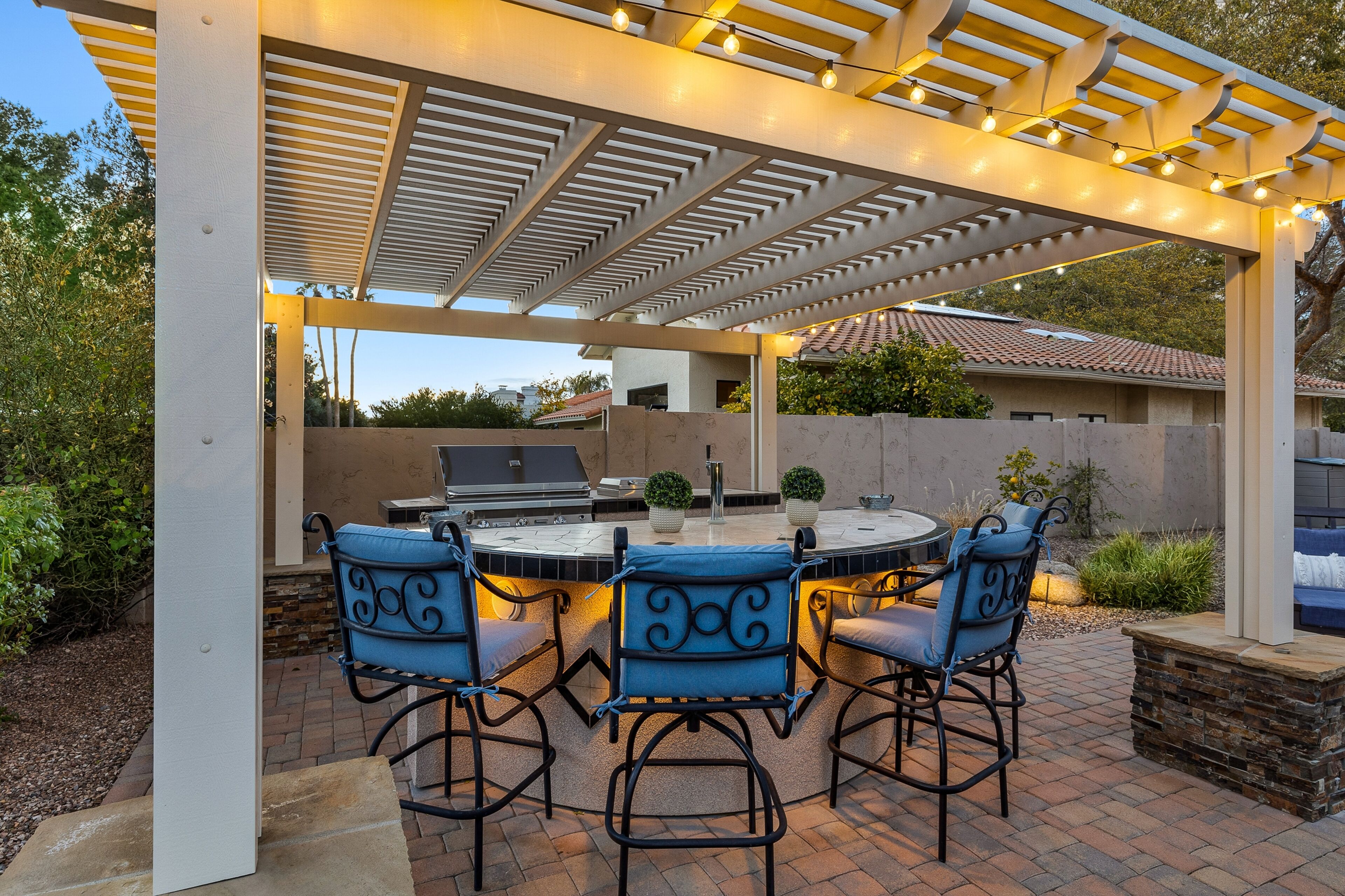 An outdoor patio with a grill, seating, and a pergola with string lights.