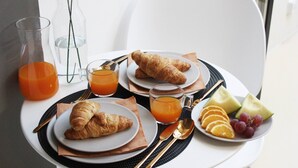 Desayuno con cruasanes, jugo y fruta sobre una mesa con una silla.