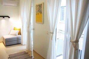 Una habitación con sofá, alfombra, una obra de arte en la pared y una puerta con cortinas.
