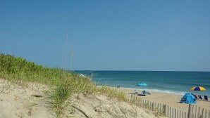 A beach with a wooden fence, beach chairs, and tents. - Beach Dugout: Semi-Oceanfront, Shared Pool (Nags Head)