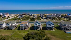 An aerial view of a coastal residential area with houses, a beach, and a clear sky. - Beach Dugout: Semi-Oceanfront, Shared Pool (Nags Head)