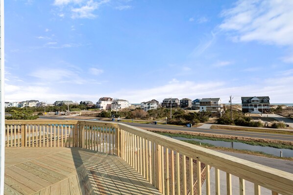 A wooden deck with a railing overlooking a residential area with houses and a road. - Beach Dugout: Semi-Oceanfront, Shared Pool (Nags Head)