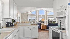 A modern kitchen with white cabinetry, a large island, and a view of the neighborhood. - Beach Dugout: Semi-Oceanfront, Shared Pool (Nags Head)