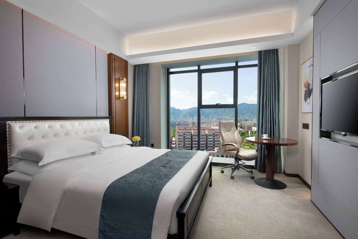 Hotelkamer met een groot bed, een bureau, een stoel, een televisie en uitzicht op de stad en de bergen.