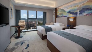 Een hotelkamer met twee bedden, een televisie, een schilderij en uitzicht op een stadsgezicht.