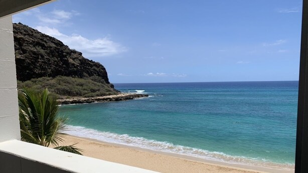 A beach with clear turquoise water, a sandy shore, and a rocky cliff. - Oceanfront condo with stunning views. Oahu’s last best kept secret (Waianae)
