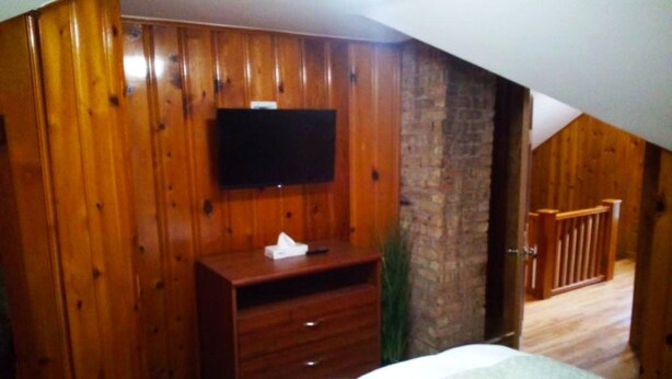 A bedroom with wooden paneling, a television mounted on the wall, a dresser, and a bed.