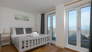 A bedroom with a bed, nightstands, a window with a view, and a painting on the wall.