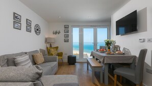 A modern living room with a grey sofa, a dining table with a polka dot tablecloth, and a TV mounted on the wall.