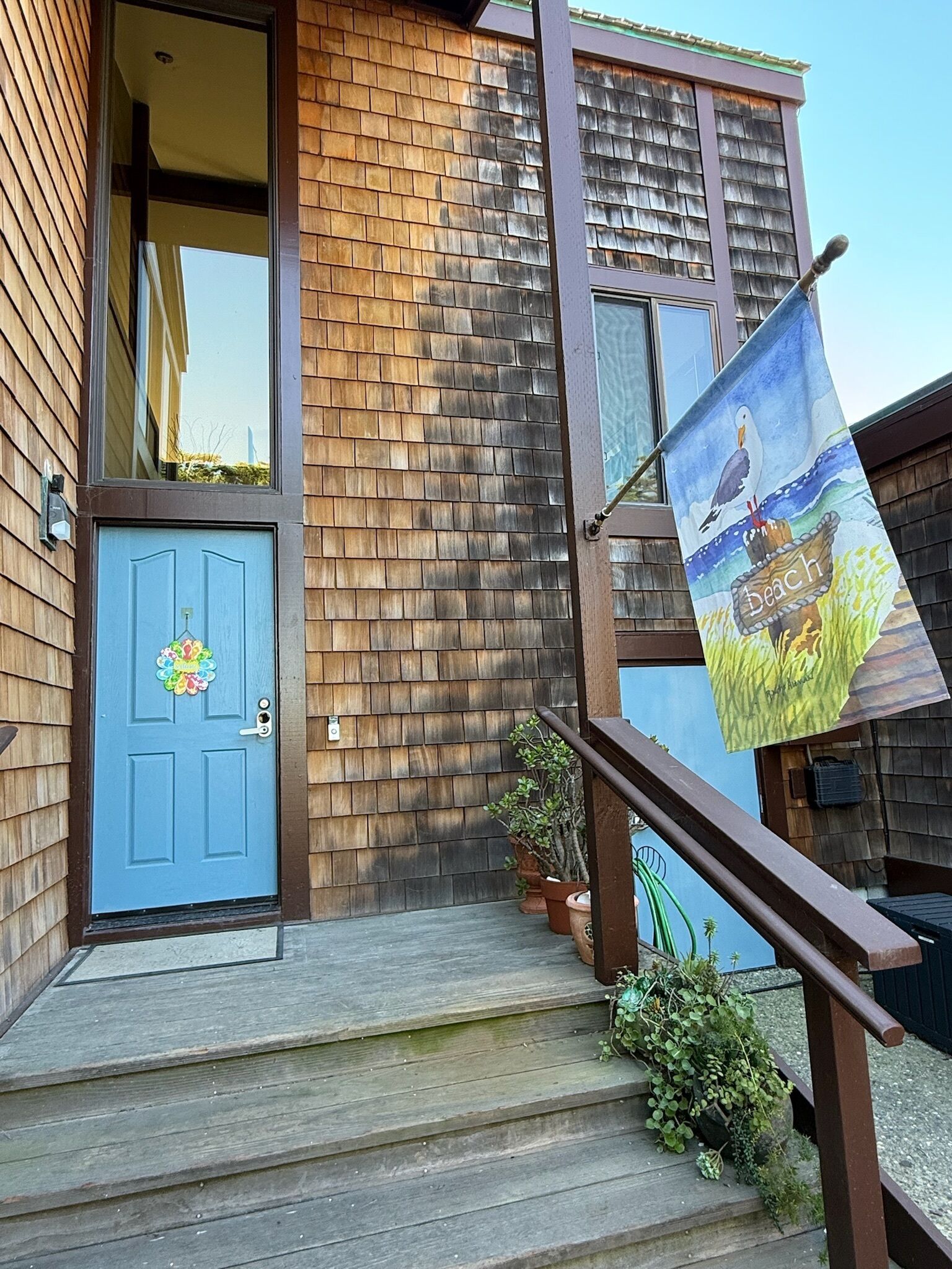 Een houten huis met een blauwe deur, een trap en een vlag met een strandafbeelding.
