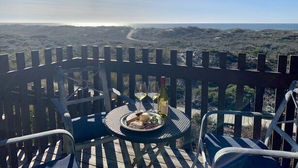 Uma mesa com uma garrafa de vinho, um copo e um prato de comida em um terraço com vista para a paisagem.