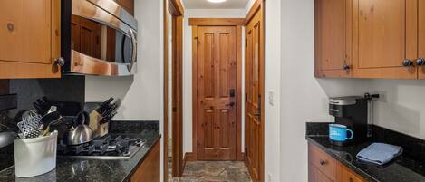 A narrow kitchen with wooden cabinets, a stainless steel stove, and a coffee maker.