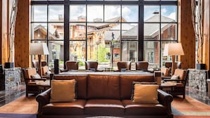 A lobby with a leather sofa, multiple chairs, a coffee table, and a large window offering a view of buildings and a stone wall.