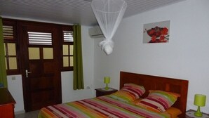 A bedroom with a bed, a nightstand, a bedside table, a door, and a wall-mounted air conditioner. - Apartment COLIBRI (Saint-Esprit)
