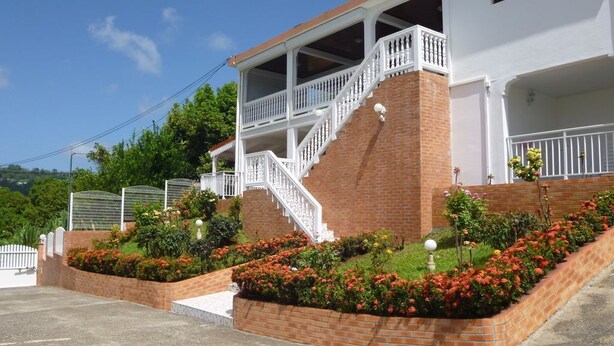 A two-story building with a white exterior, a brick base, and a balcony with white railings. - Apartment COLIBRI (Saint-Esprit)