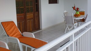 A balcony with white chairs and orange cushions, a wooden door, and a small table with a vase of flowers. - Apartment COLIBRI (Saint-Esprit)
