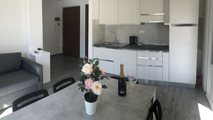 A modern kitchen with white cabinets, a dining table with a vase of flowers, and a bottle of champagne. - Sant'antonino Apartments - Maestrale (levanto)